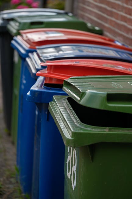 A close-up view of a collection of crushed aluminum beverage cans, including silver cans with pull-tab tops, some with partially visible branding such as Coca-Cola, and others with various colors and 